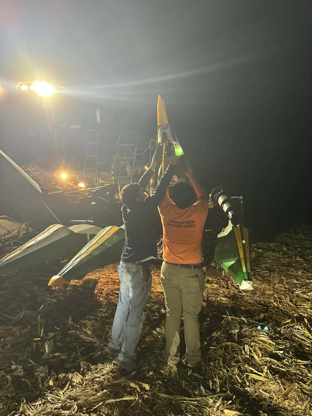 Two crew members working on the corn head at night